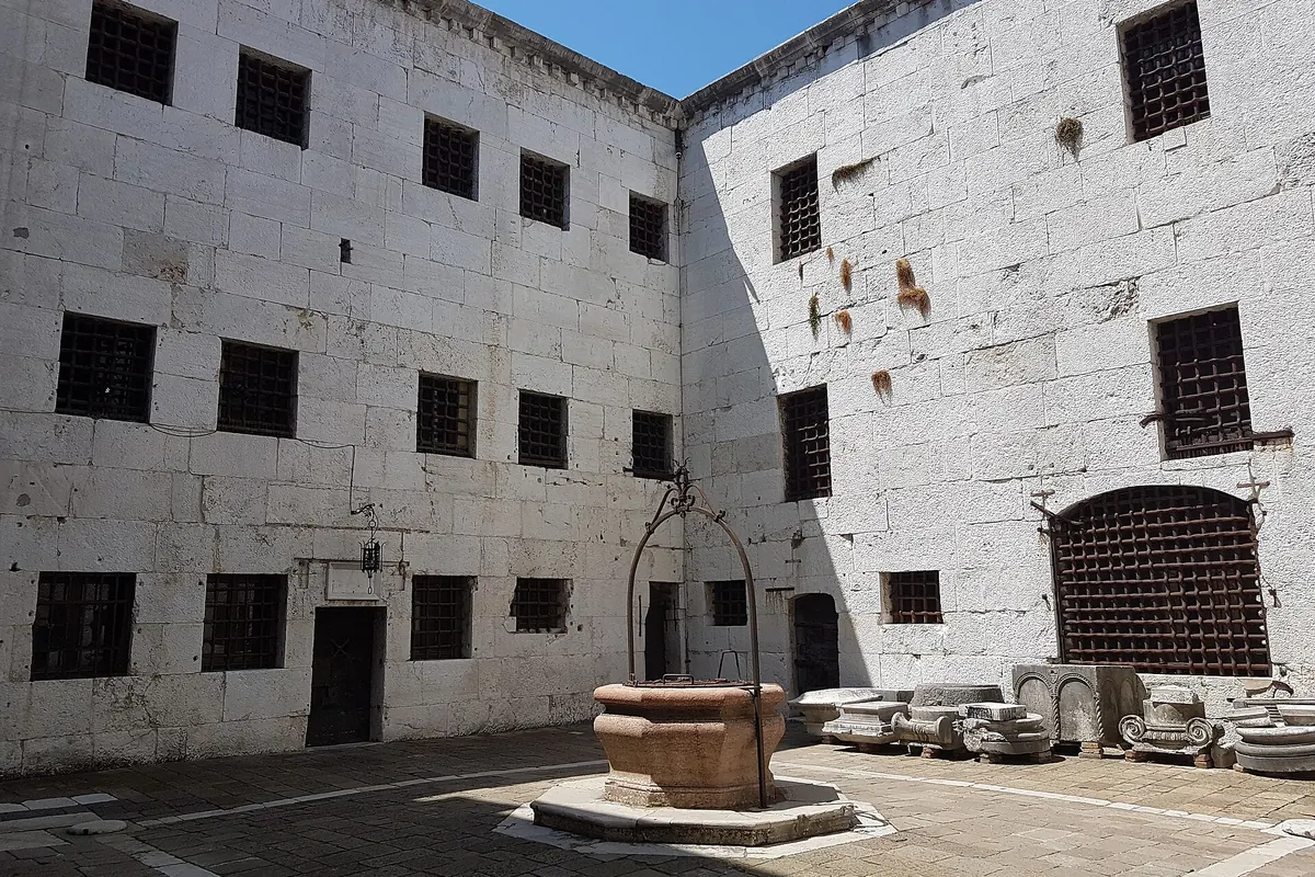The inner courtyard of the New Prisons, with white stone walls, rows of small barred windows and a well head in the middle.